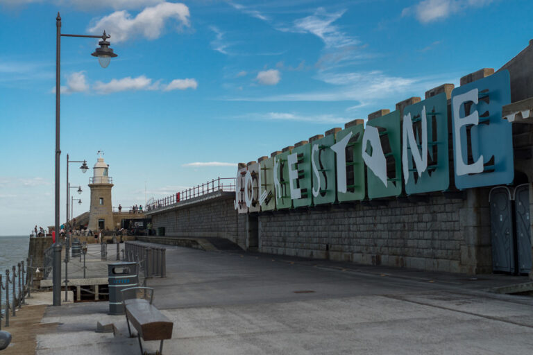 Unterwegs - der neue Hafen in Folkestone mit der Promenade und dem neuen Schild auf dem steht Folkestone, bei strahlendem blauen Himmel.